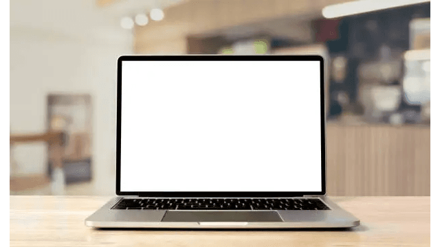 A laptop with a blank white screen placed on a wooden table in a cafe setting.