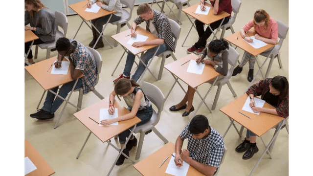 A classroom full of diverse students diligently taking notes or exams at individual desks.