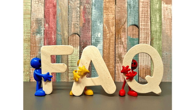 Colorful toy figures interact with wooden letters spelling "FAQ" against a rustic wooden background.