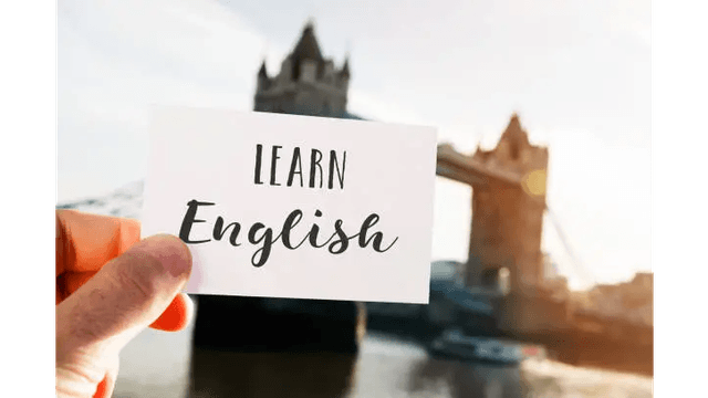 A hand holds a card saying "LEARN English" with the Tower Bridge in the background.